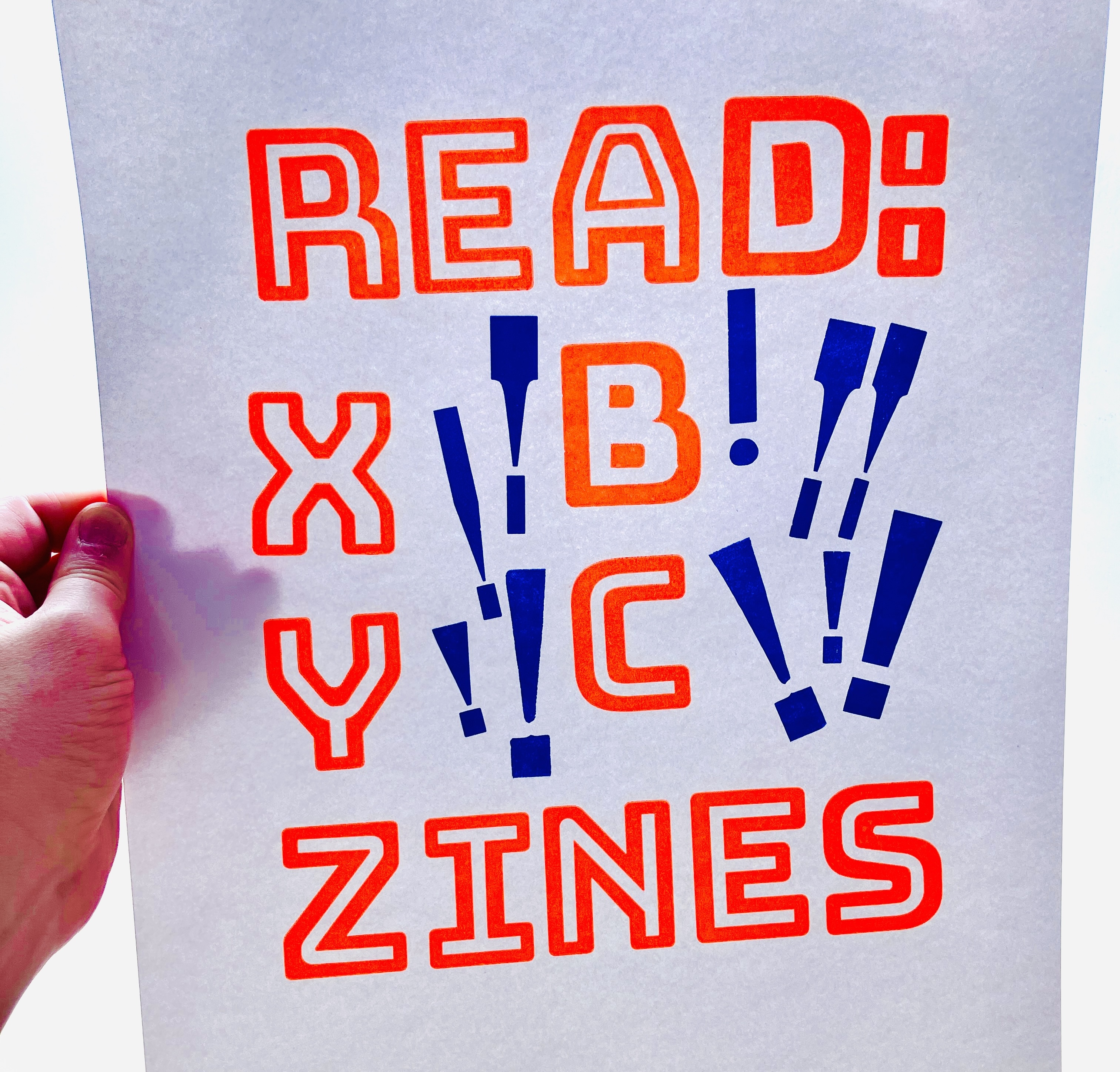Photo of a letterpress print on bright white paper with bright dayglo orange ink and dark blue-purple ink. The dayglo orange ink says "Read: Zines" in all caps, with the letters "ABC" dropping off "read"'s A, and "XYZ" stacking above "zines"'s Z. It's a chunky, playful, irregular inline font. Around that orange text are a variety of dark blue-purple exclamation marks from various wood-type fonts. The print is held up by a hand in front of a frosted-glass door through which soft light is glowing. The print has extra white paper at the bottom in this photo, as I only cut it down to final size after taking this photo.